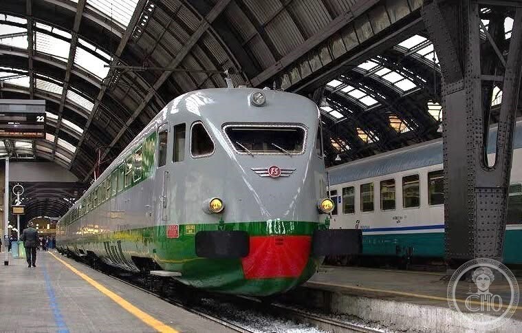 A preserved streamlined Italian railcar in grey, green and red livery at a station platform under an iron and glass roof