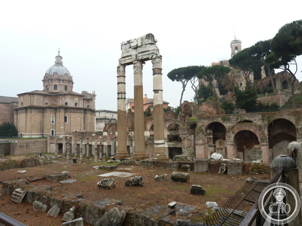 Three Corinthian columns on a high podium among low ruins, a baroque church with a dome on the left and umbrella pines behind
