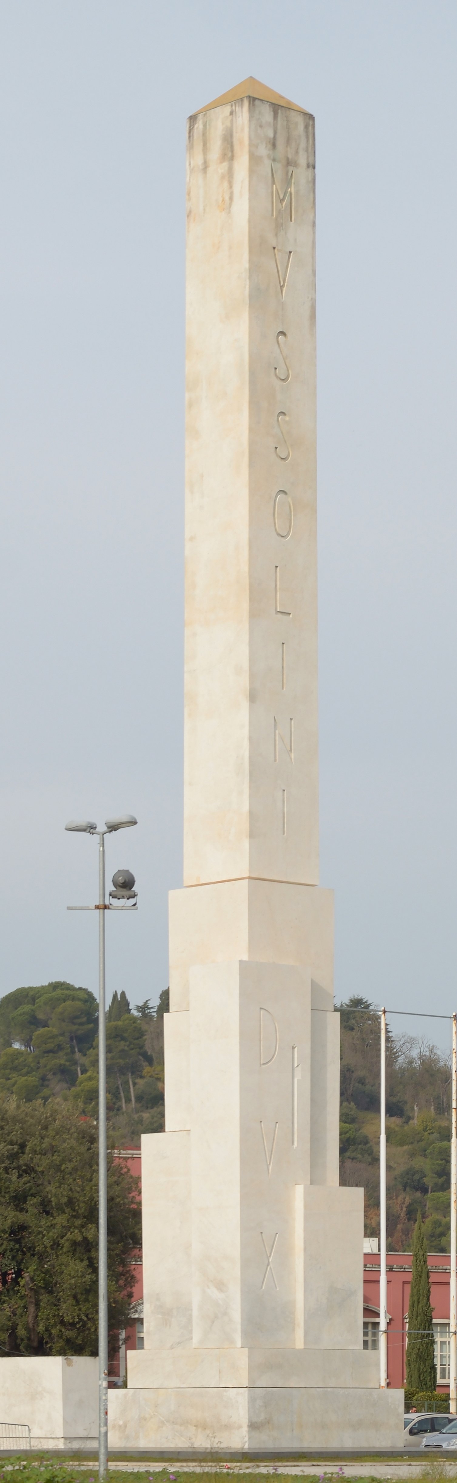 The white Carrara marble monolith known as the Obelisco del Foro Italico rising at the entrance of the Roman sports complex