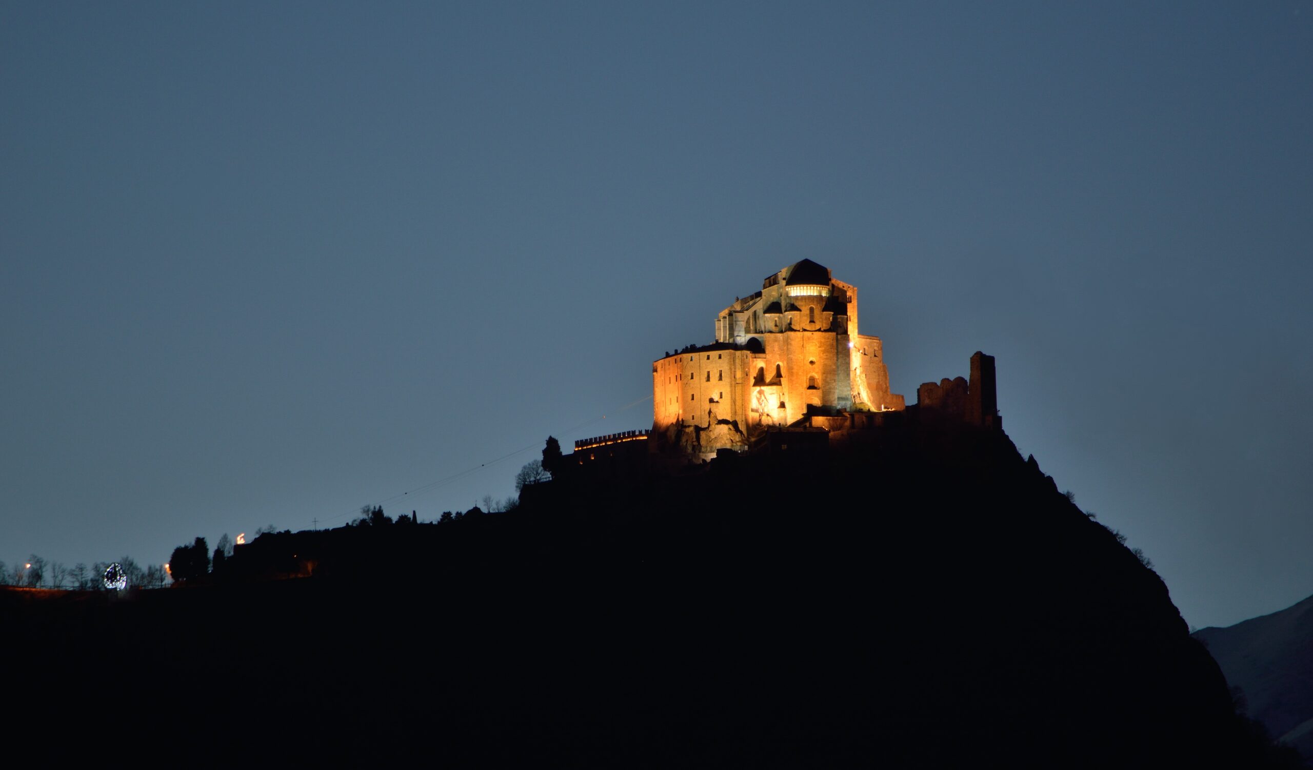 Sacra di San Michele illuminated at blue hour, silhouetted against the twilight sky on Monte Pirchiriano