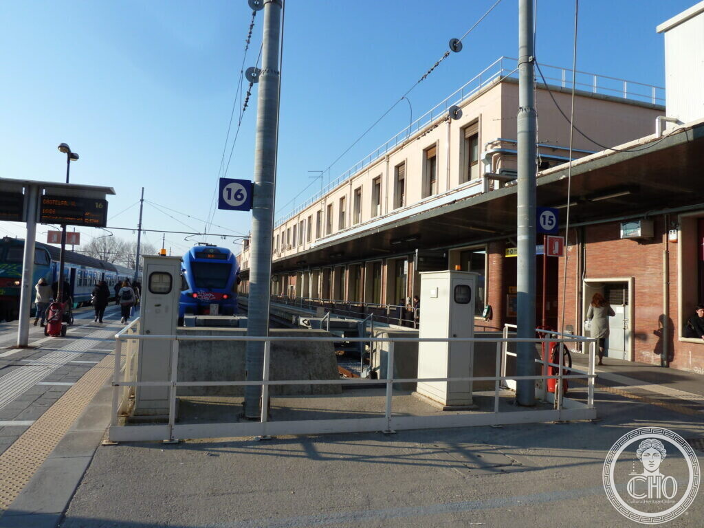 Railway platforms numbered 15 and 16 with trains, overhead wires and a long pale station building on the right