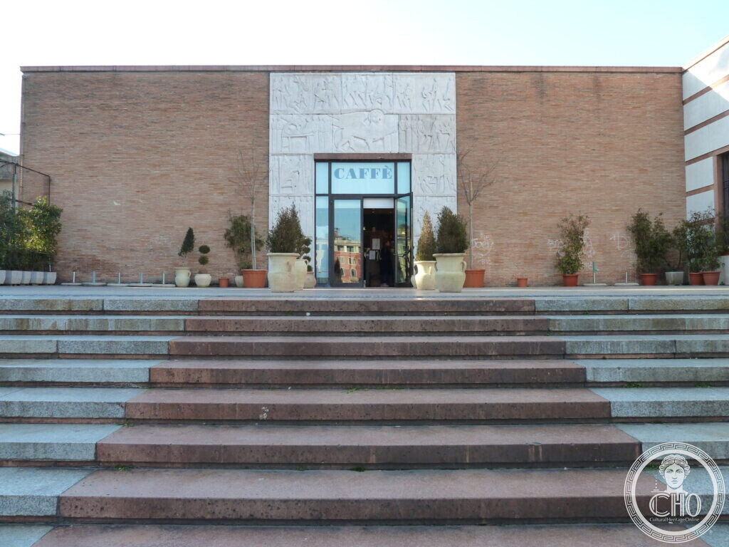 Wide stone steps leading up to a plain brick building block with a carved stone frame around its glazed doorway