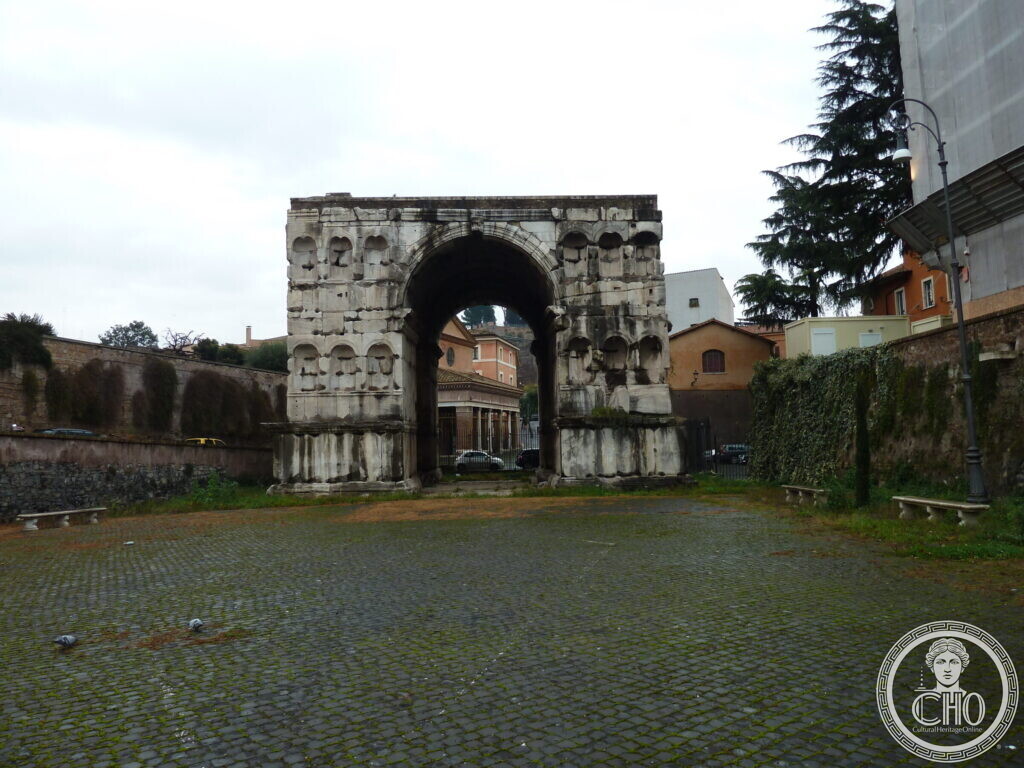 Massive marble arch on four piers with rows of empty niches on its faces, on a cobbled square