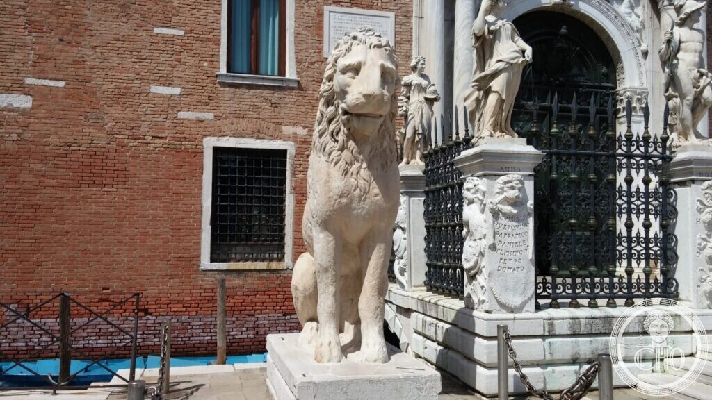 A tall seated white marble lion on a pedestal beside the carved stone gate of the Arsenal