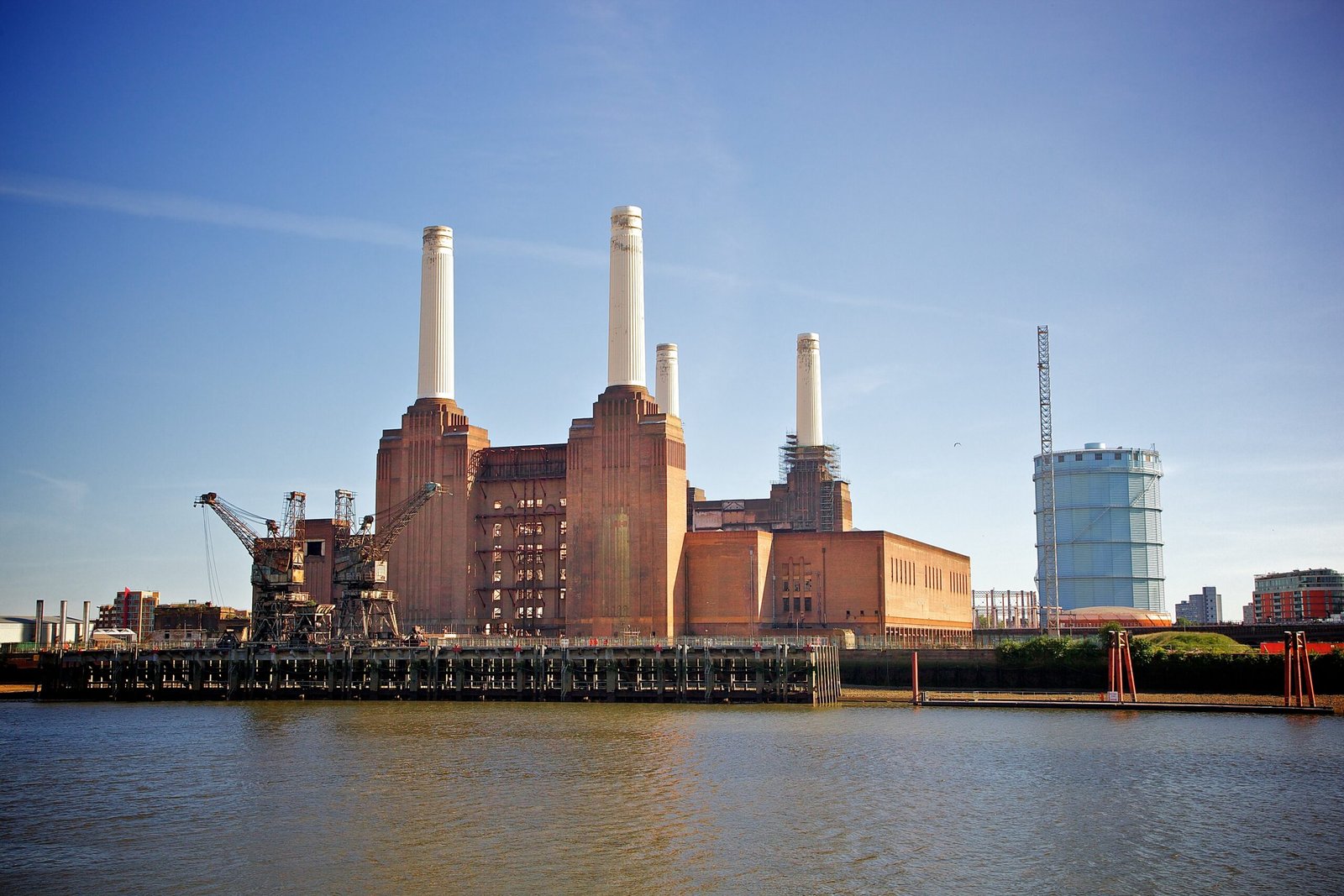 Battersea Power Station in London with its four white chimneys above brick walls beside the Thames