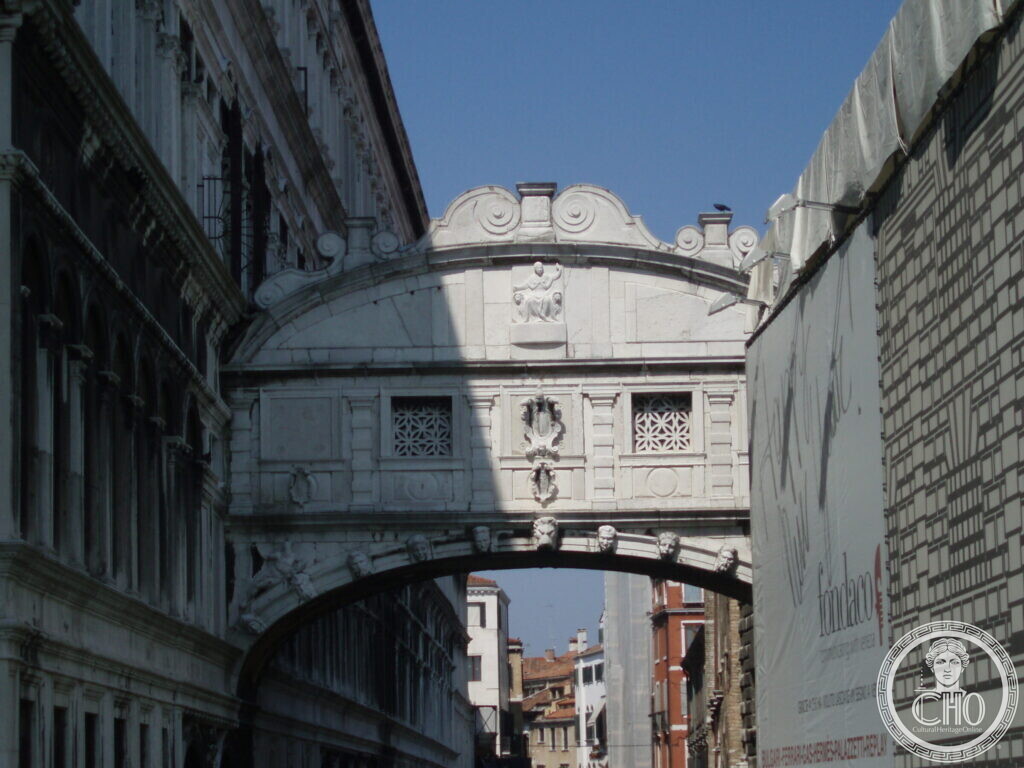 Enclosed white marble bridge with carved decoration and two small barred windows, spanning a narrow canal between two palaces