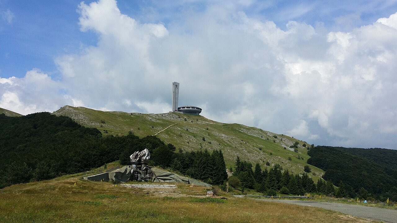 The Buzludzha Monument, a vast concrete flying-saucer structure rising from the Balkan Mountains summit, photographed from the approach road