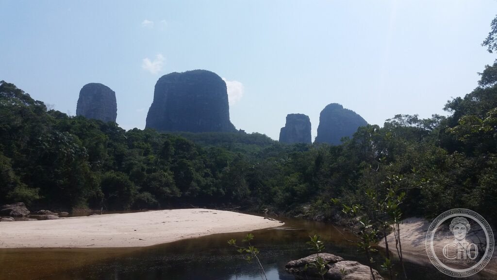 Table-topped tepui rocks rising above Amazon rainforest and a river beach in Chiribiquete, Colombia
