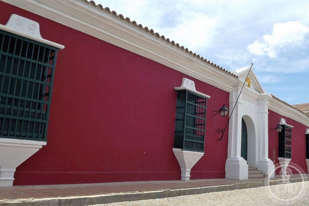 A long red-and-white colonial earthen building on a cobbled street in the historic town of Coro