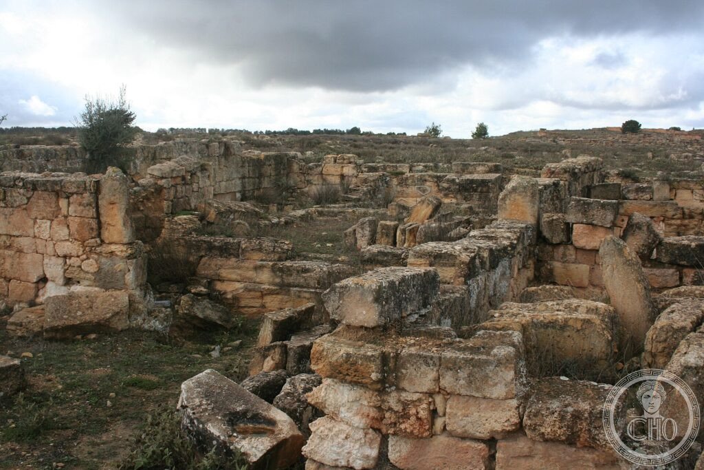 Weathered ancient stone ruins and fallen blocks on the hillside of Cyrene under a cloudy sky, Libya