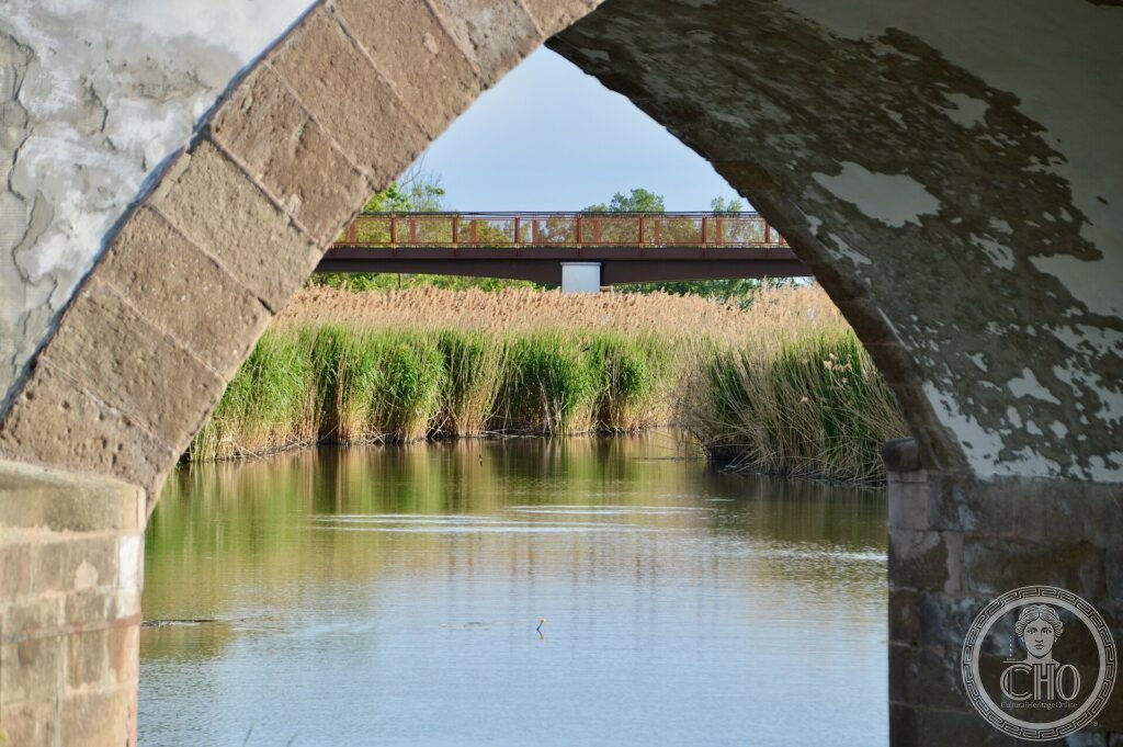 The stone Nine-arch bridge of Hortobágy reflected in calm water amid the reeds of the puszta