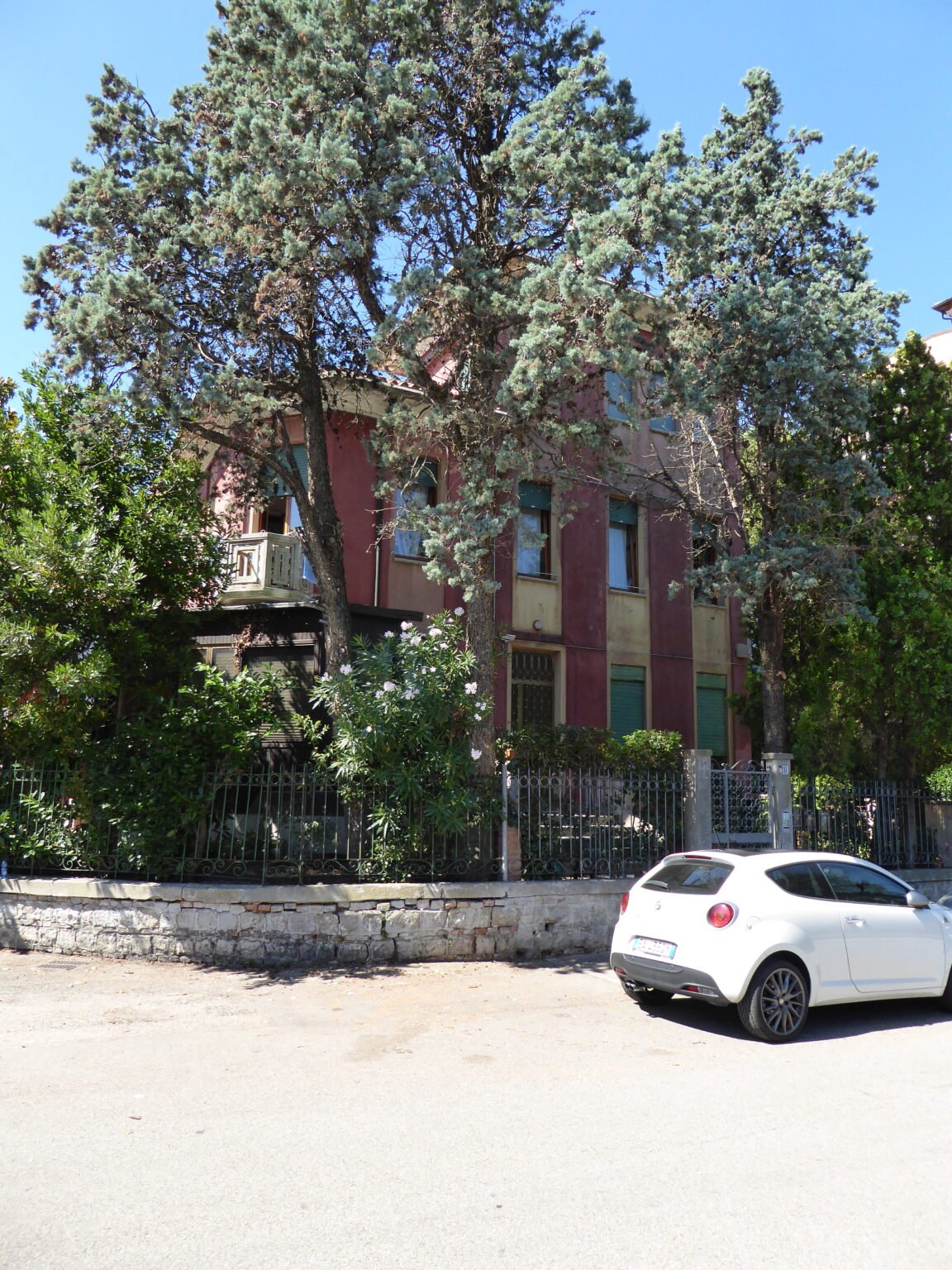 Villino Faido on the Lido di Venezia, a brick and plaster villa set behind a large conifer and an iron railing
