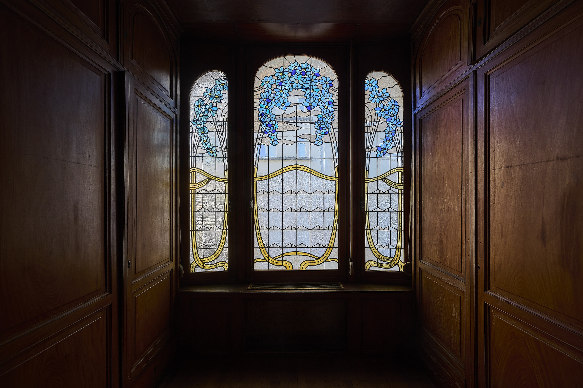 Stained-glass bay window of the Maison Hannon with blue flowers set in wood panelling
