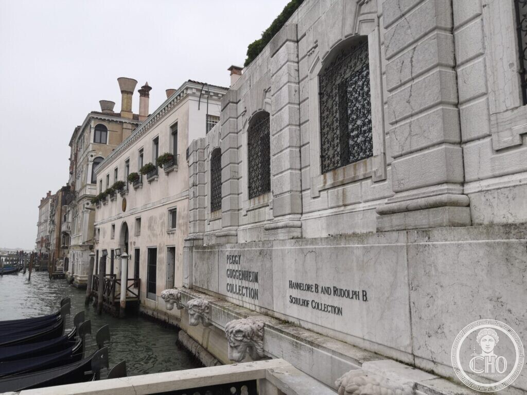 The white stone base of Palazzo Venier dei Leoni on the Grand Canal, with carved lion heads and engraved collection names, gondolas moored below