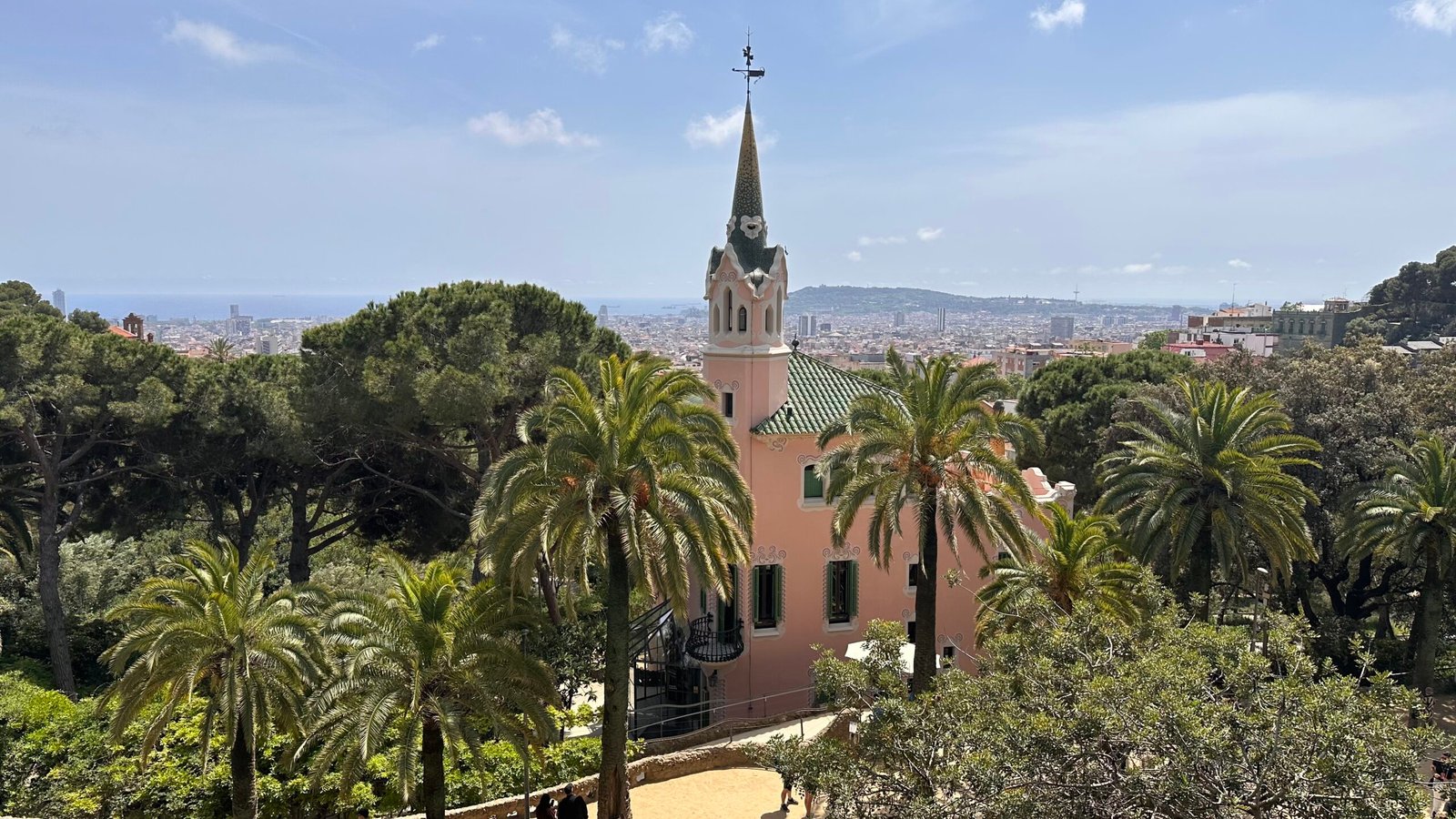 The pink-towered Gaudí House Museum among palm trees in Park Güell, with Barcelona behind