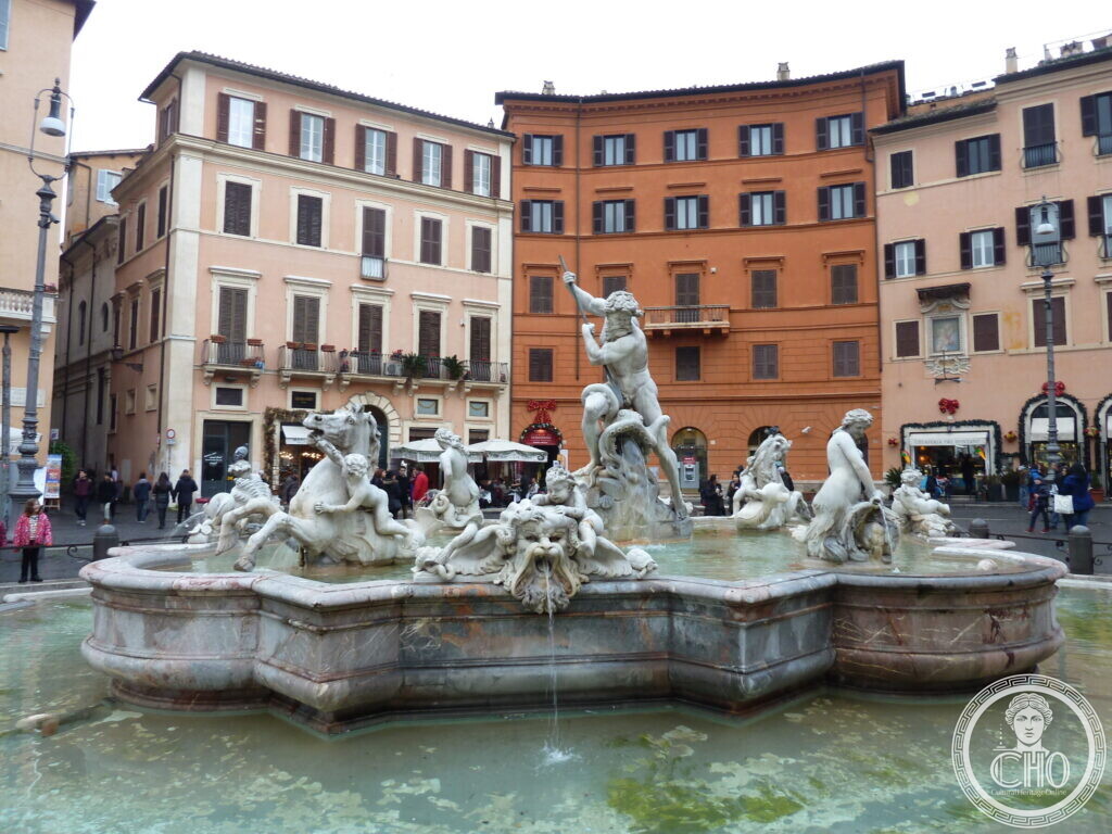 Marble fountain group in a basin, orange and ochre house fronts and shop awnings behind