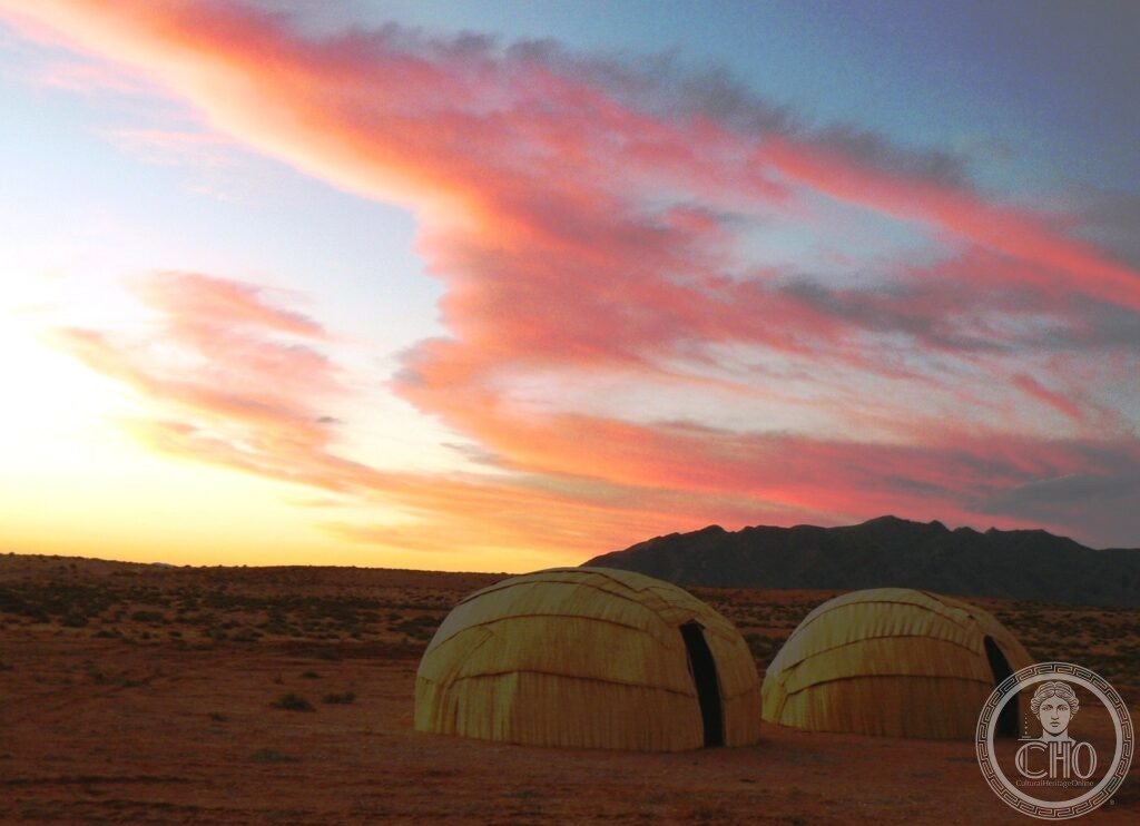 Two domed Nama reed huts (matjieshuis) in the desert at sunset, with mountains behind, Richtersveld