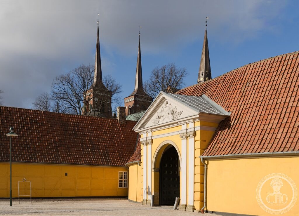 The red-brick twin spires of Roskilde Cathedral rising behind a yellow gatehouse