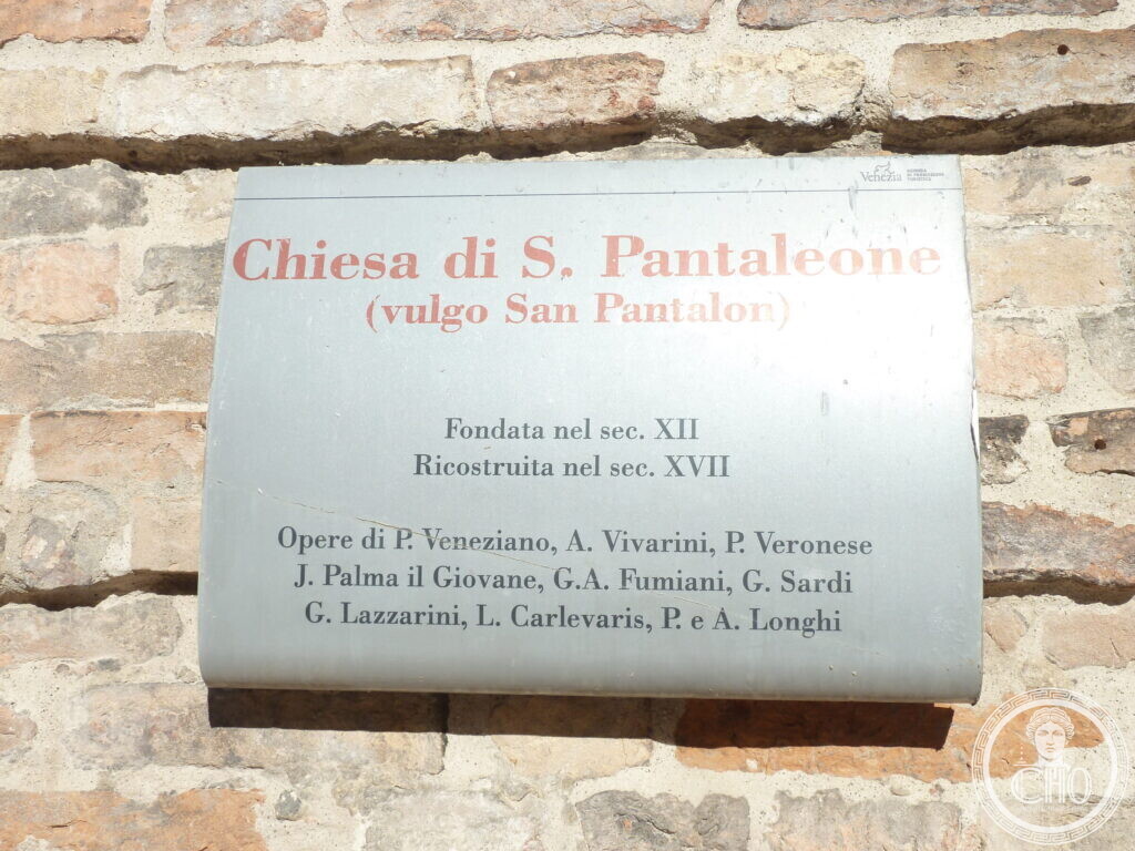 A metal information plate on a brick wall reading Chiesa di S. Pantaleone, vulgo San Pantalon, founded in the 12th century and rebuilt in the 17th