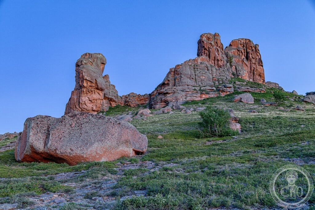 Red rock outcrops rising from the green spring steppe of central Kazakhstan