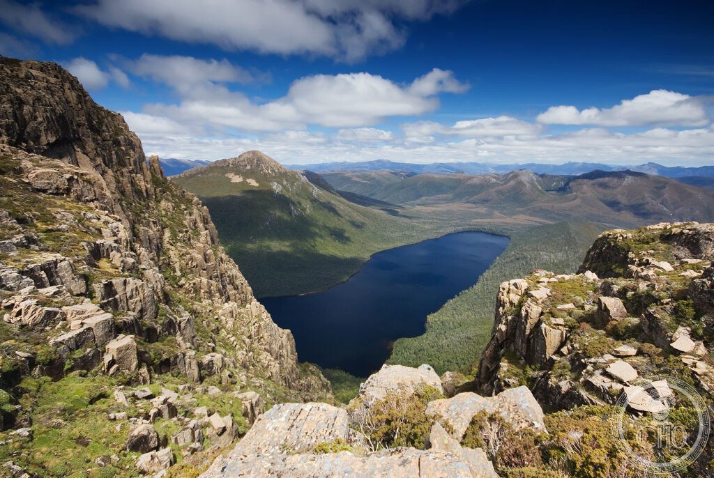 A deep blue glacial lake set among rugged forested mountains in the Tasmanian Wilderness