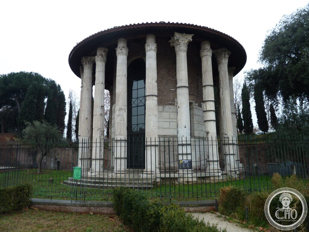 The same round temple from another side, the cella door visible between the columns, cypresses and a lawn behind