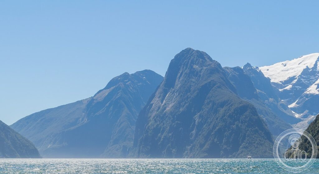 A steep peak rising sheer from the water of Milford Sound fjord, with snow and forested cliffs