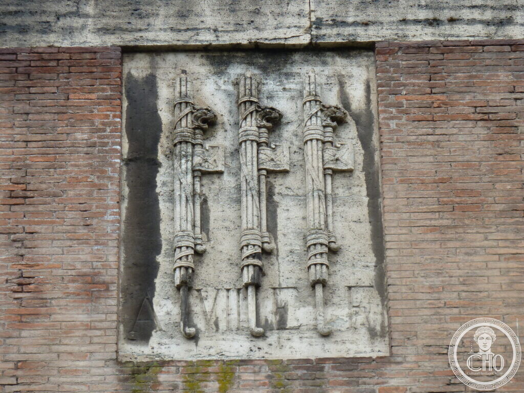 Rectangular marble relief carved with three bundles of rods bound together, set into a brick wall