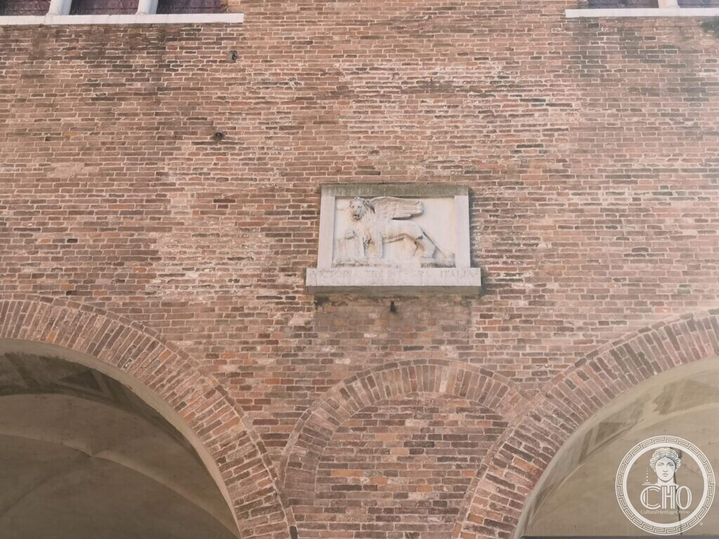 A small white stone relief of the winged lion of Saint Mark set in a brick wall above two arches