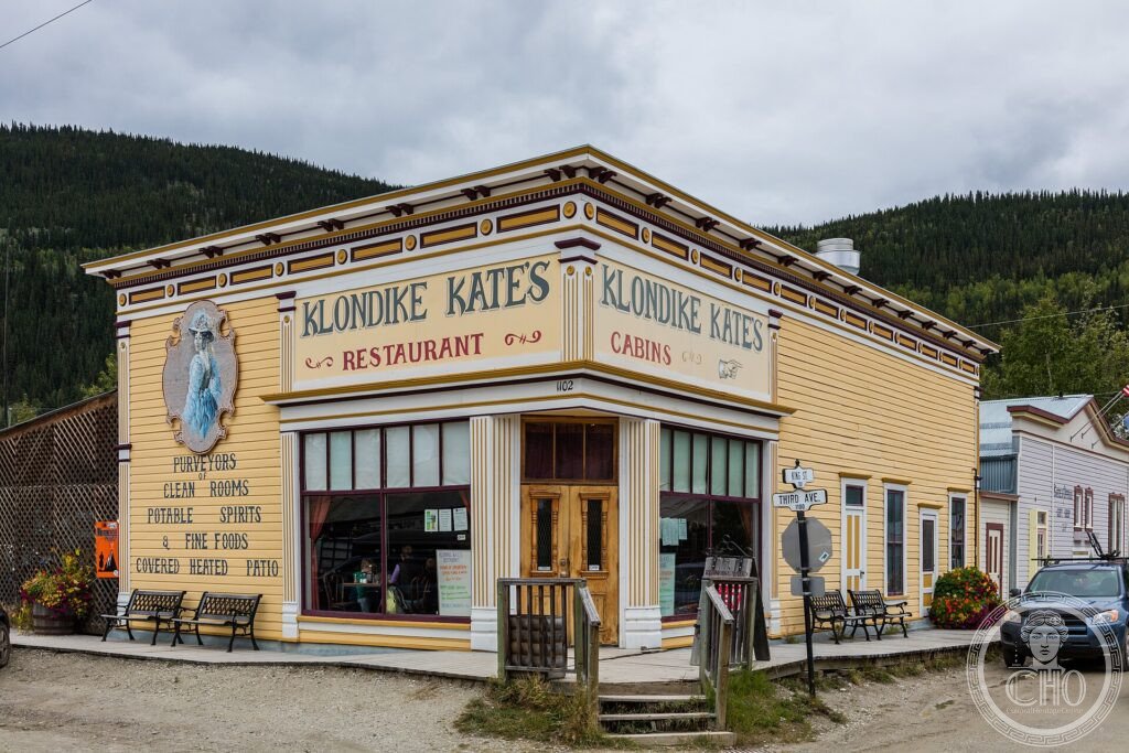A restored yellow gold-rush era building, Klondike Kate's, on a dirt street in Dawson City, Yukon