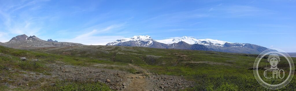 The snow-and-ice cap of Vatnajökull rising above green heathland and a gravel trail in Iceland