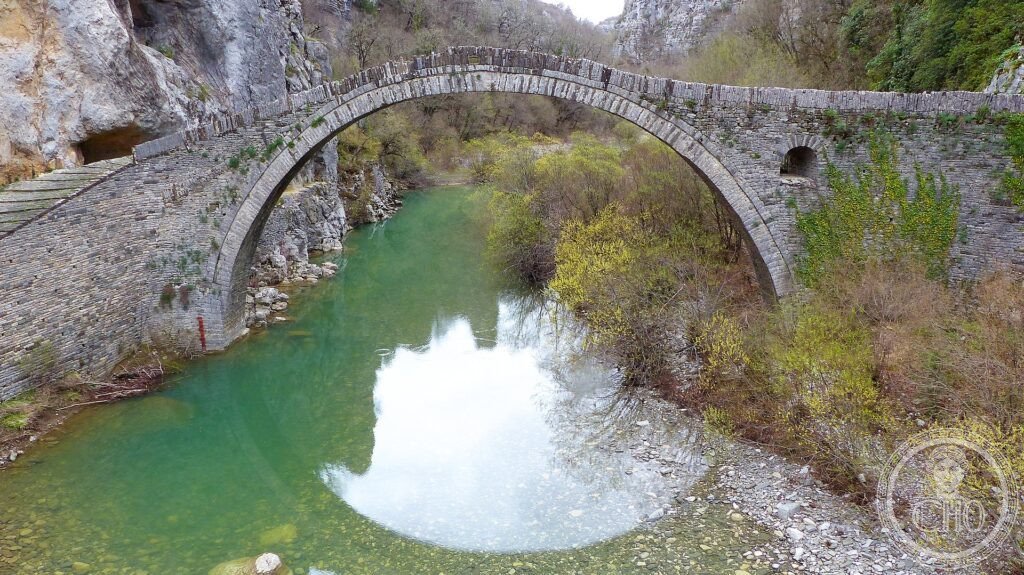 A graceful old stone arched bridge over a clear river among the green mountains of Zagori, Greece
