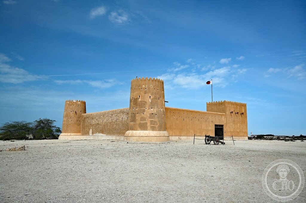 The restored ochre walls and corner towers of Al Zubarah Fort under a blue sky in the Qatari desert