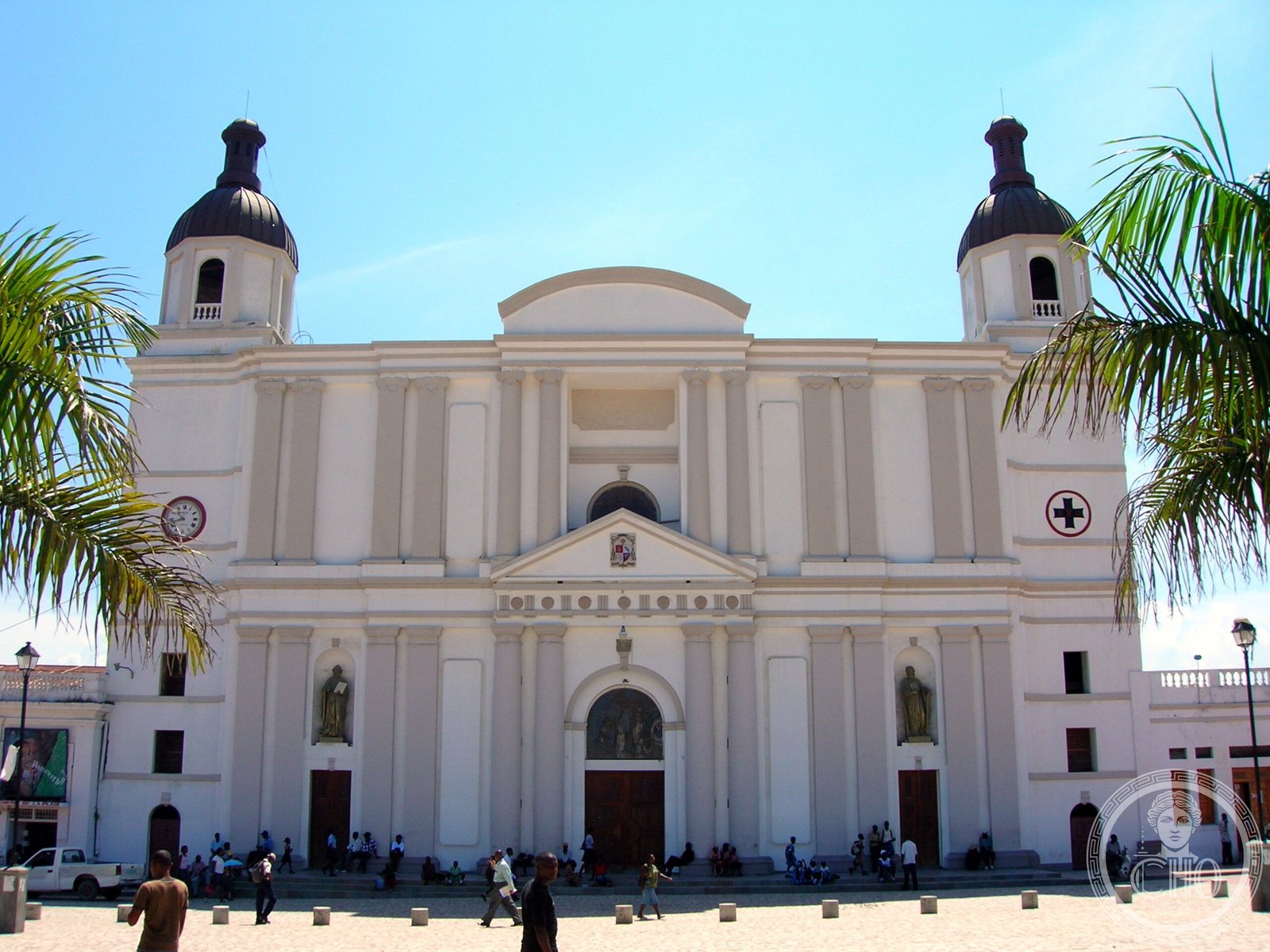 Cathedral of Notre-Dame de l'Assomption in Cap-Haïtien, Haiti, a white colonial-style facade with twin dark-domed bell towers flanked by palm trees