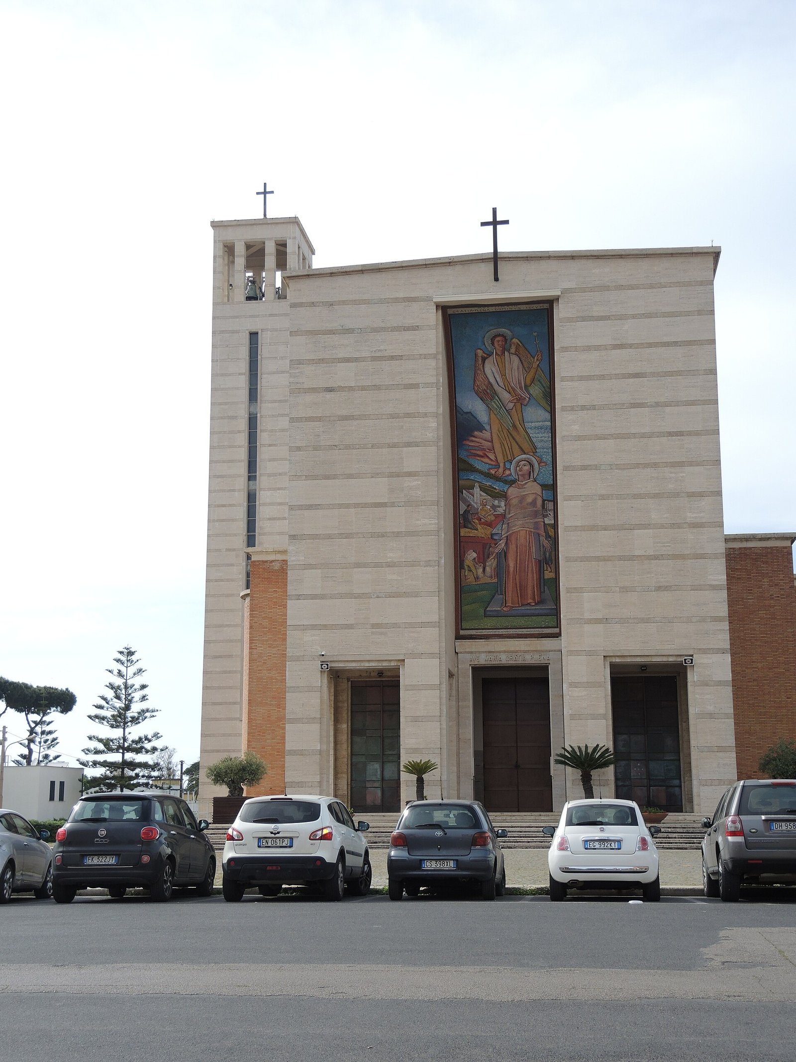 The travertine facade of the church of the Santissima Annunziata in Sabaudia, with the tall vertical mosaic of the Annunciation and the bell tower