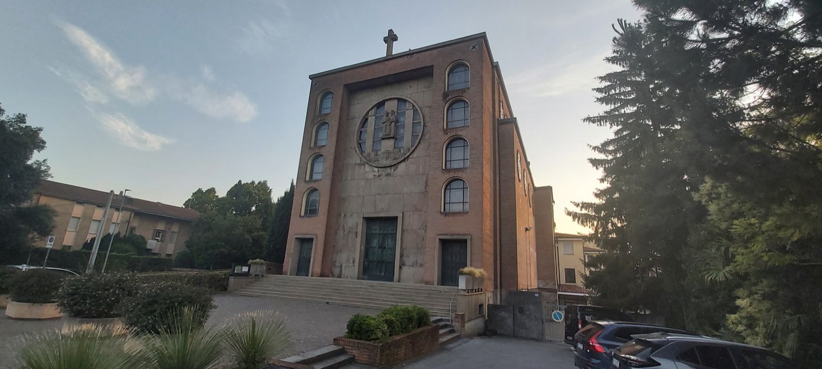 Brick and stone facade of the Sacra Famiglia church in Padua, with a large circular relief in the gable