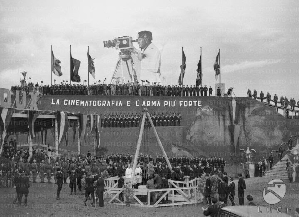 Rome 1937, the ceremony for the laying of the first stone of Cinecitta, filmed by Istituto Luce, with a backdrop reading La cinematografia e l'arma piu forte