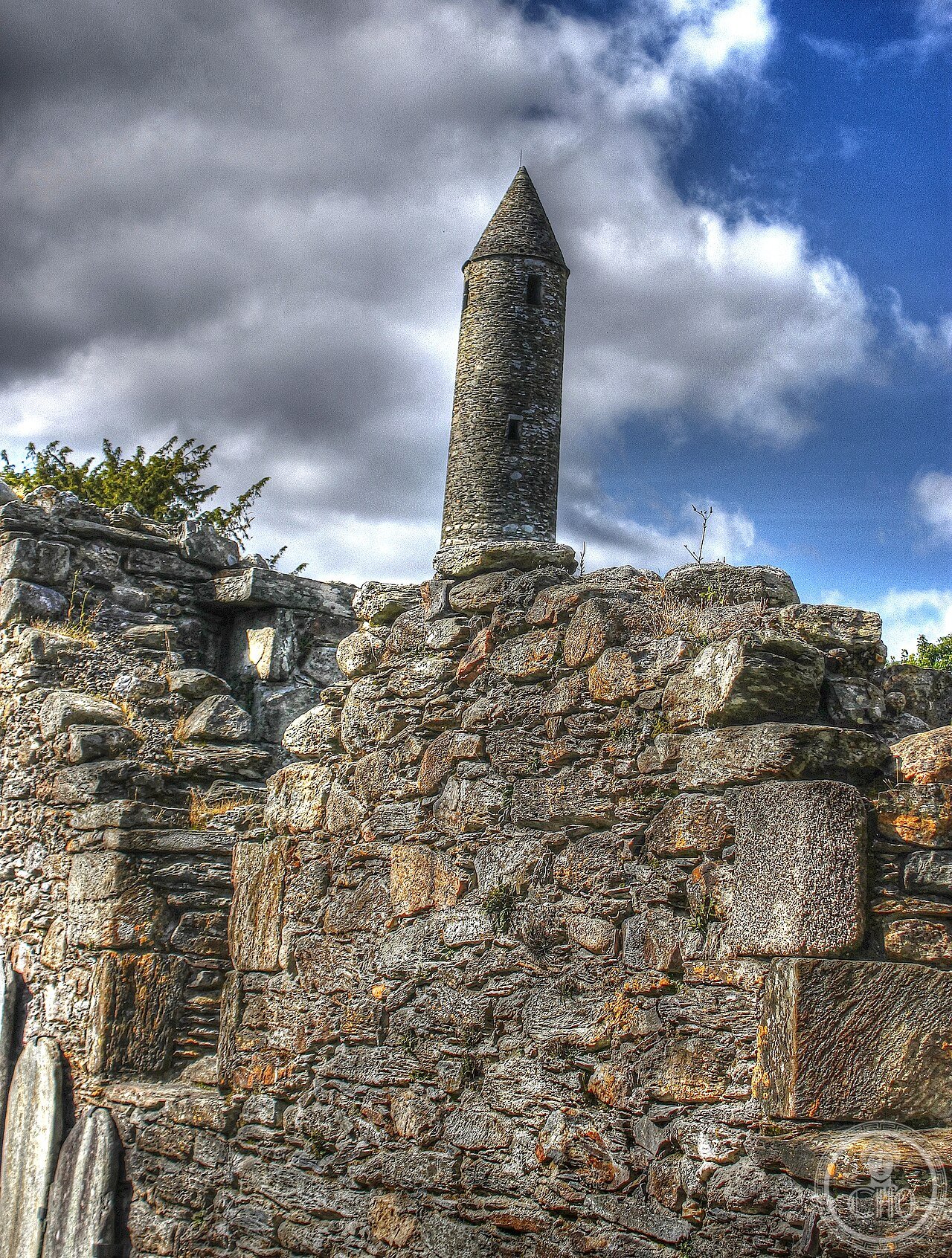 Round tower and ruined wall at Glendalough monastic site, County Wicklow, Ireland, founded in the 6th century by Saint Kevin in the Valley of the Two Lakes