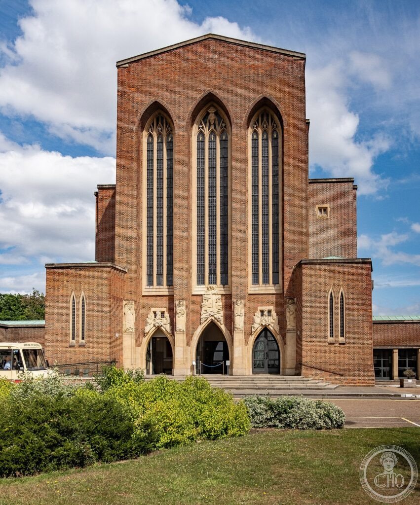 Red brick Gothic Revival west front of Guildford Cathedral rising above Stag Hill