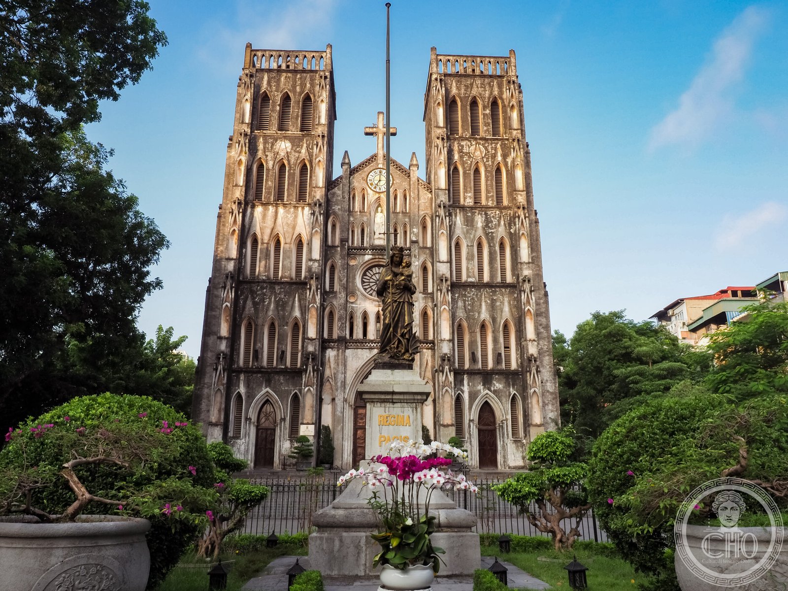 St. Joseph's Cathedral, Hanoi, a neo-Gothic facade with twin bell towers photographed at golden hour with a Madonna statue and flowers in the foreground