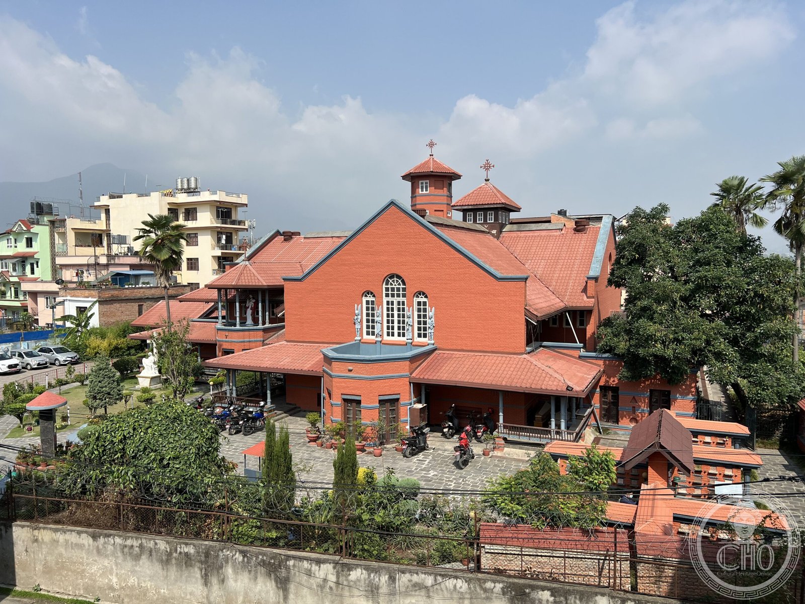Assumption Cathedral in Kathmandu Valley, Nepal, a red-brick church with twin octagonal towers, seen from above with motorbikes parked in the forecourt