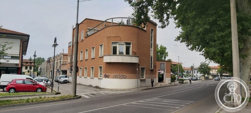 A brick building with a curved corner and a projecting balcony at a road junction, a pedestrian crossing in front