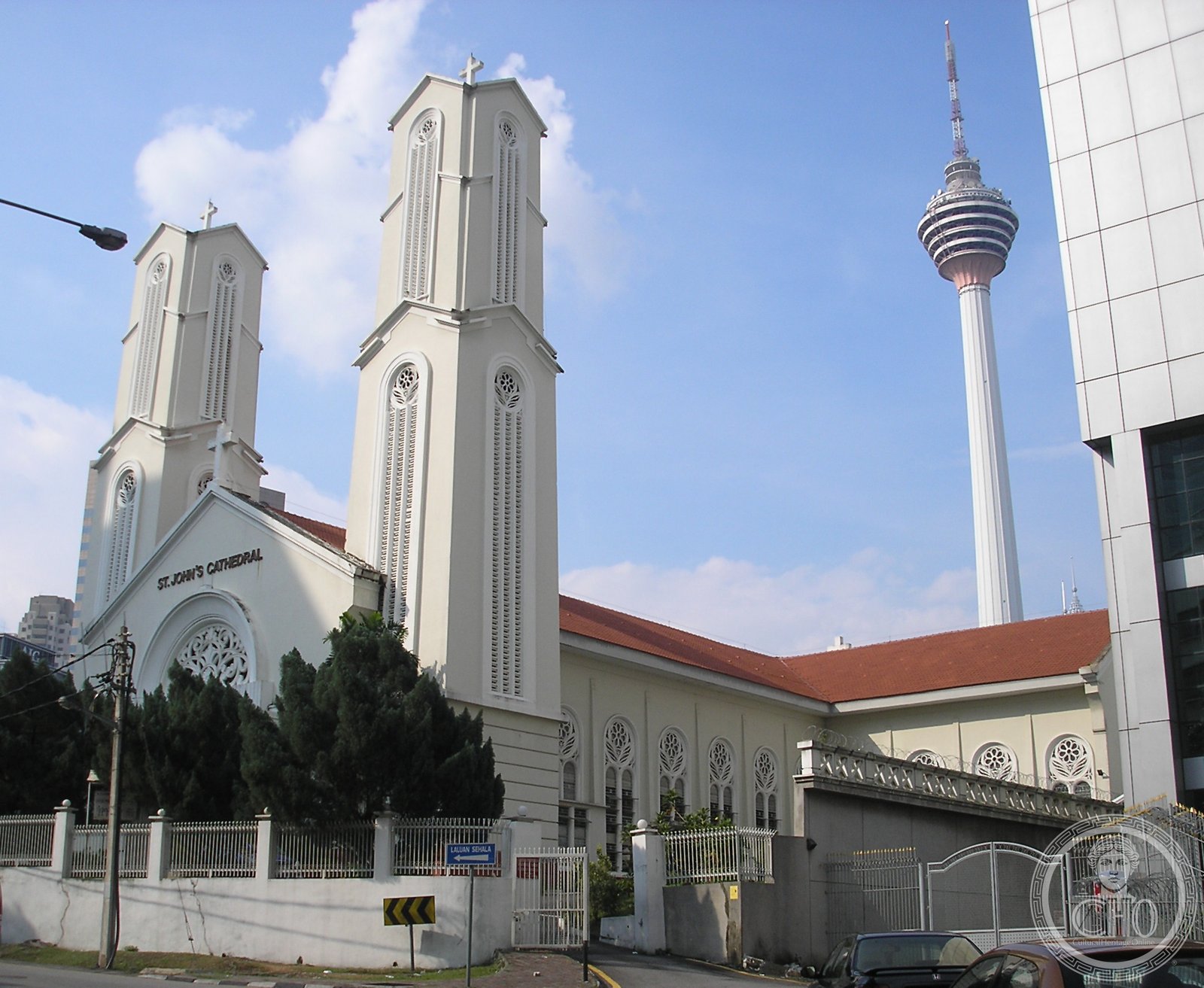 Cathedral of St. John the Evangelist in Kuala Lumpur, Malaysia, a white Grecian-Spanish style facade with red-tiled roof, the Kuala Lumpur Tower visible behind
