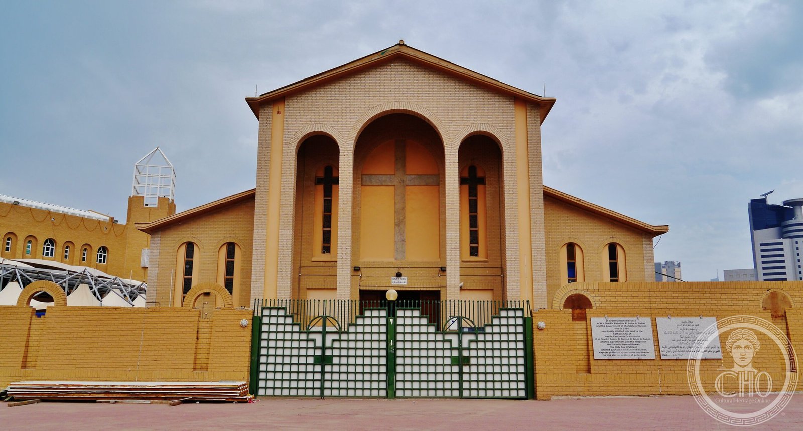 Holy Family Co-Cathedral in Kuwait City, Kuwait, a sand-colored Catholic church built 1957-1961, its 1966 land-grant plaque naming the Emir visible on the gate