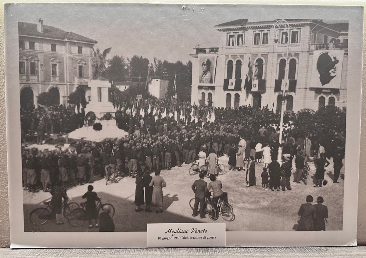 A crowd filling Piazza dei Caduti at Mogliano Veneto on 10 June 1940, with large portraits of Mussolini on the buildings