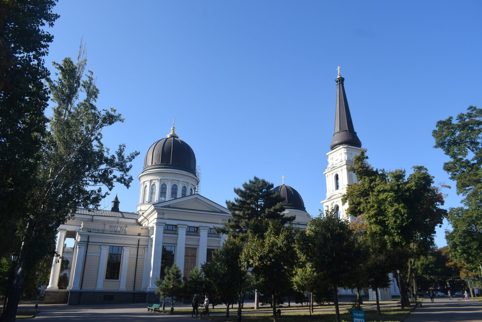 The white Neoclassical Transfiguration Cathedral of Odesa with its black domes and tall bell tower, on tree-lined Cathedral Square, before the 2023 damage