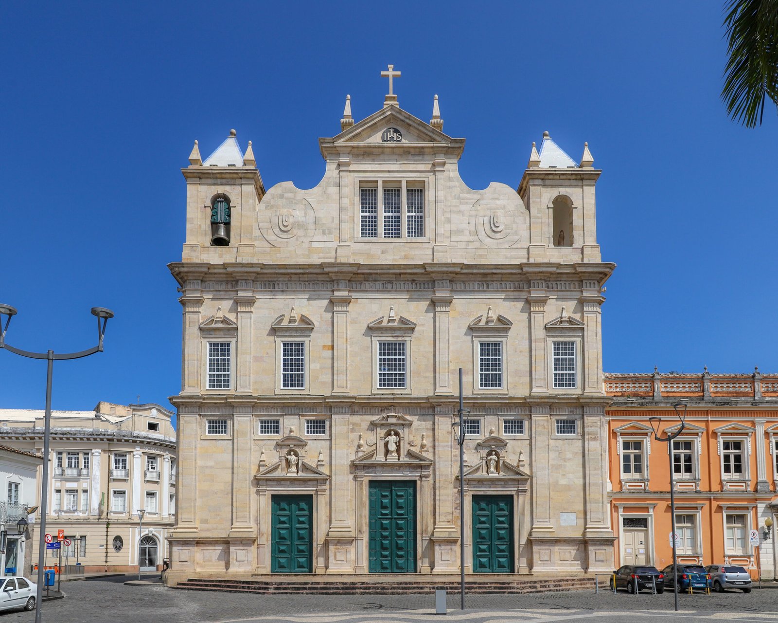 Pale lioz-limestone facade of the Cathedral Basilica of Salvador, with twin towers, scrolled pediment and the Jesuit IHS monogram, on the Terreiro de Jesus