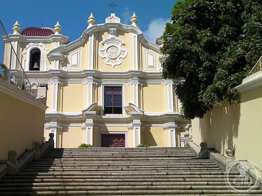 St. Joseph's Seminary and Church, Macau, a yellow-ochre baroque facade with white pilasters and a distinctive reddish dome topped by a weathervane, seen from its monumental staircase