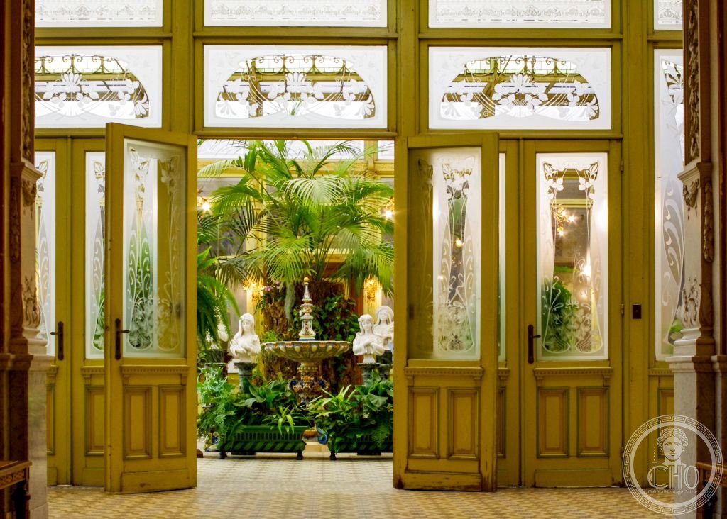 Etched Art Nouveau glass doors opening onto the Winter Garden of the Ursulines, with palm trees and a fountain visible beyond
