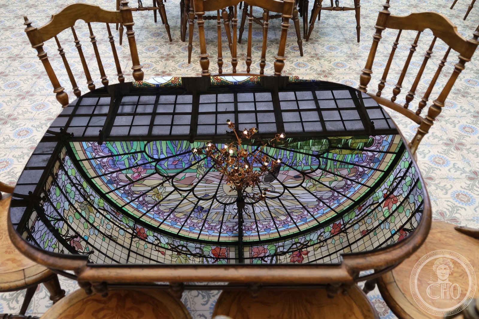 The leaded-glass vault of the Winter Garden of the Ursulines reflected in a polished table top among period chairs